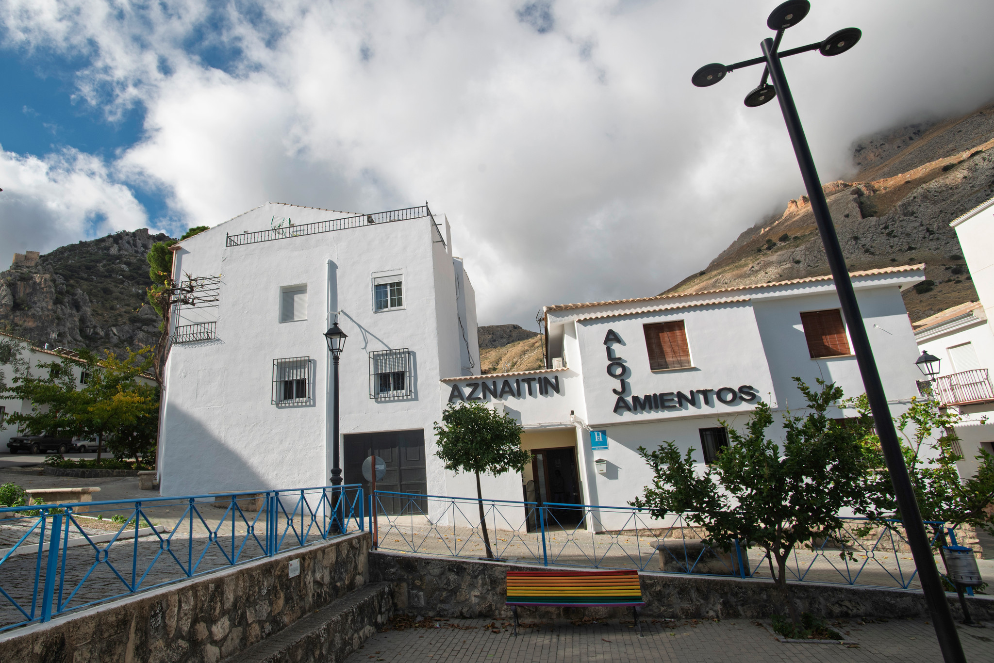 Fachada del Hostal Pico Aznaitín, con su característico caserío blanco integrado en el entorno del pueblo y las montañas al fondo, que refuerzan su conexión con la sierra.