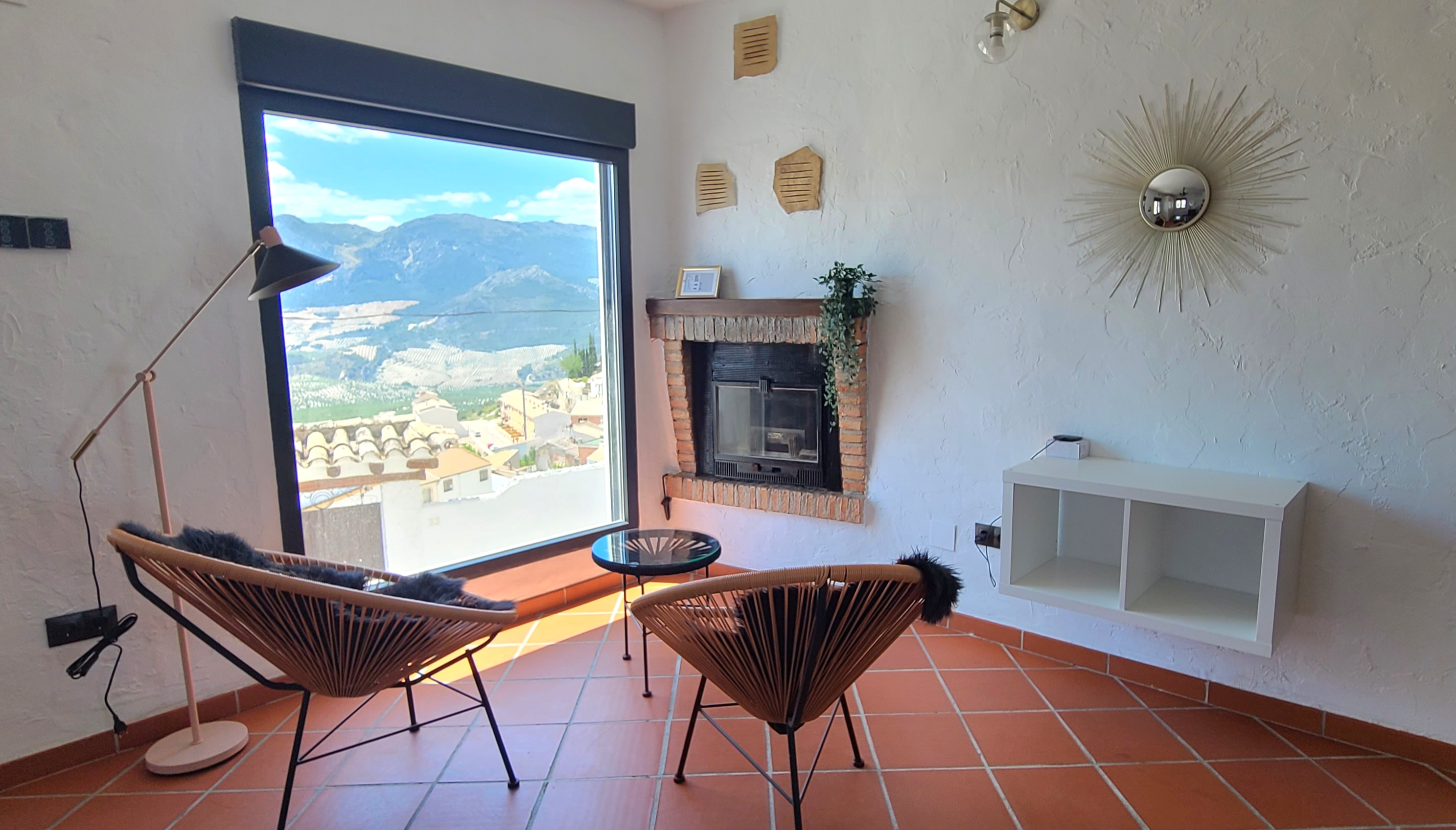 Rincón luminoso con gran ventanal panorámico que enmarca el paisaje de montaña y el caserío. Dos sillones invitan a la pausa junto a la chimenea, en un espacio pensado para contemplar y relajarse. La combinación de materiales naturales y líneas sencillas aporta equilibrio y confort.