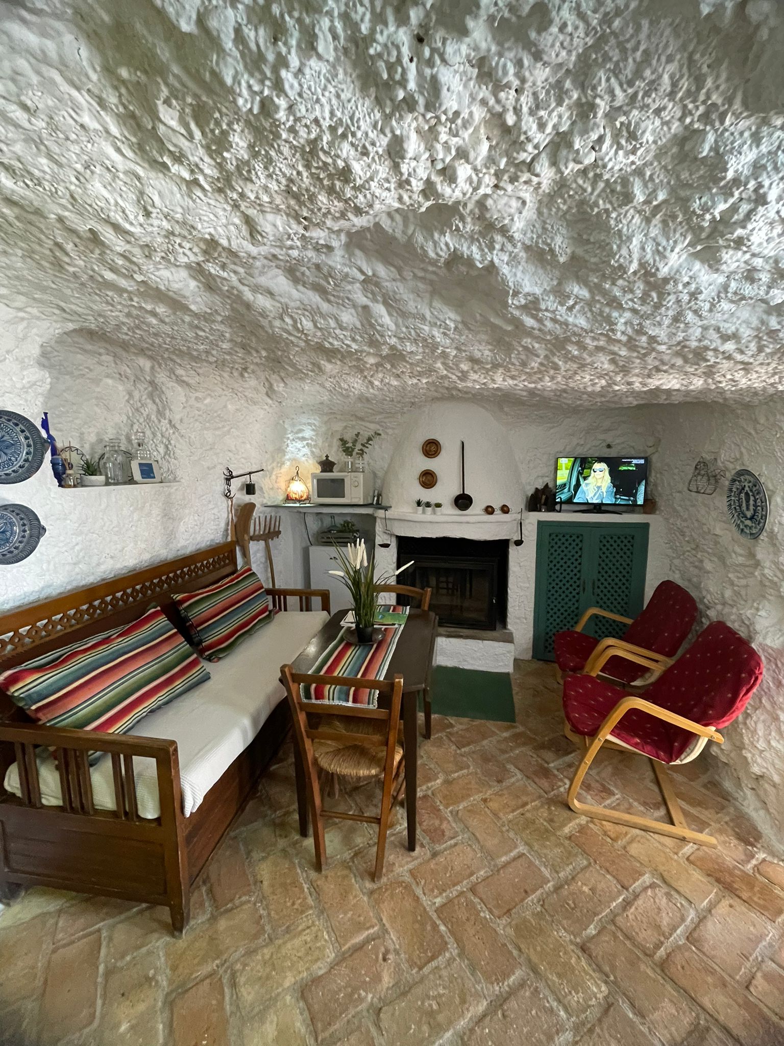 Salón acogedor excavado en la roca, con mobiliario sencillo y detalles tradicionales. La chimenea y los textiles aportan calidez en un entorno pensado para el descanso.