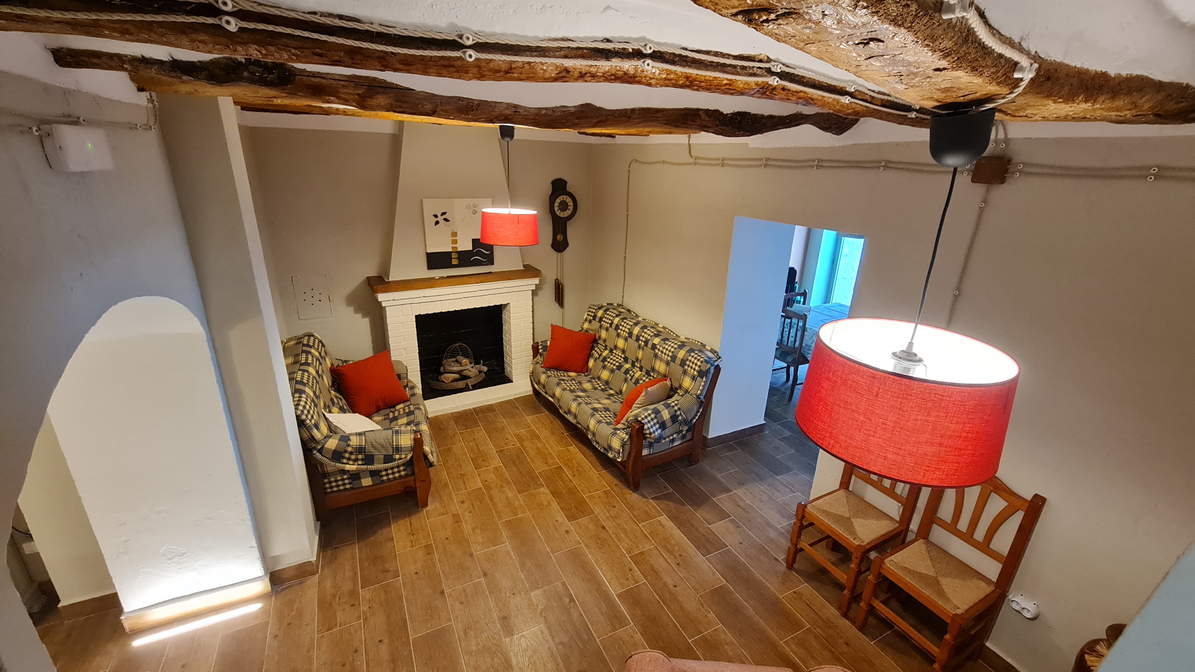 Salón de ambiente tradicional, con vigas de madera, chimenea y sofás tapizados. La iluminación y los materiales refuerzan una sensación de calidez y recogimiento.