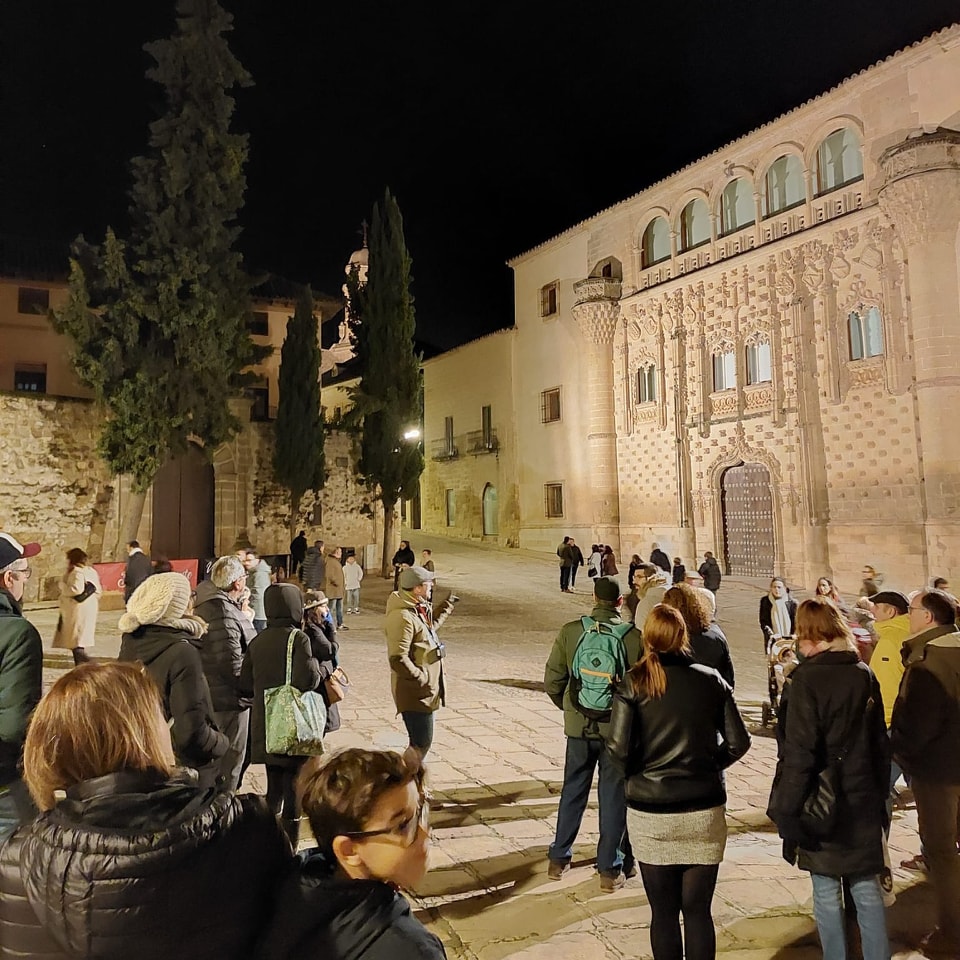 Grupo de visitantes durante una ruta guiada junto a un edificio histórico iluminado.
