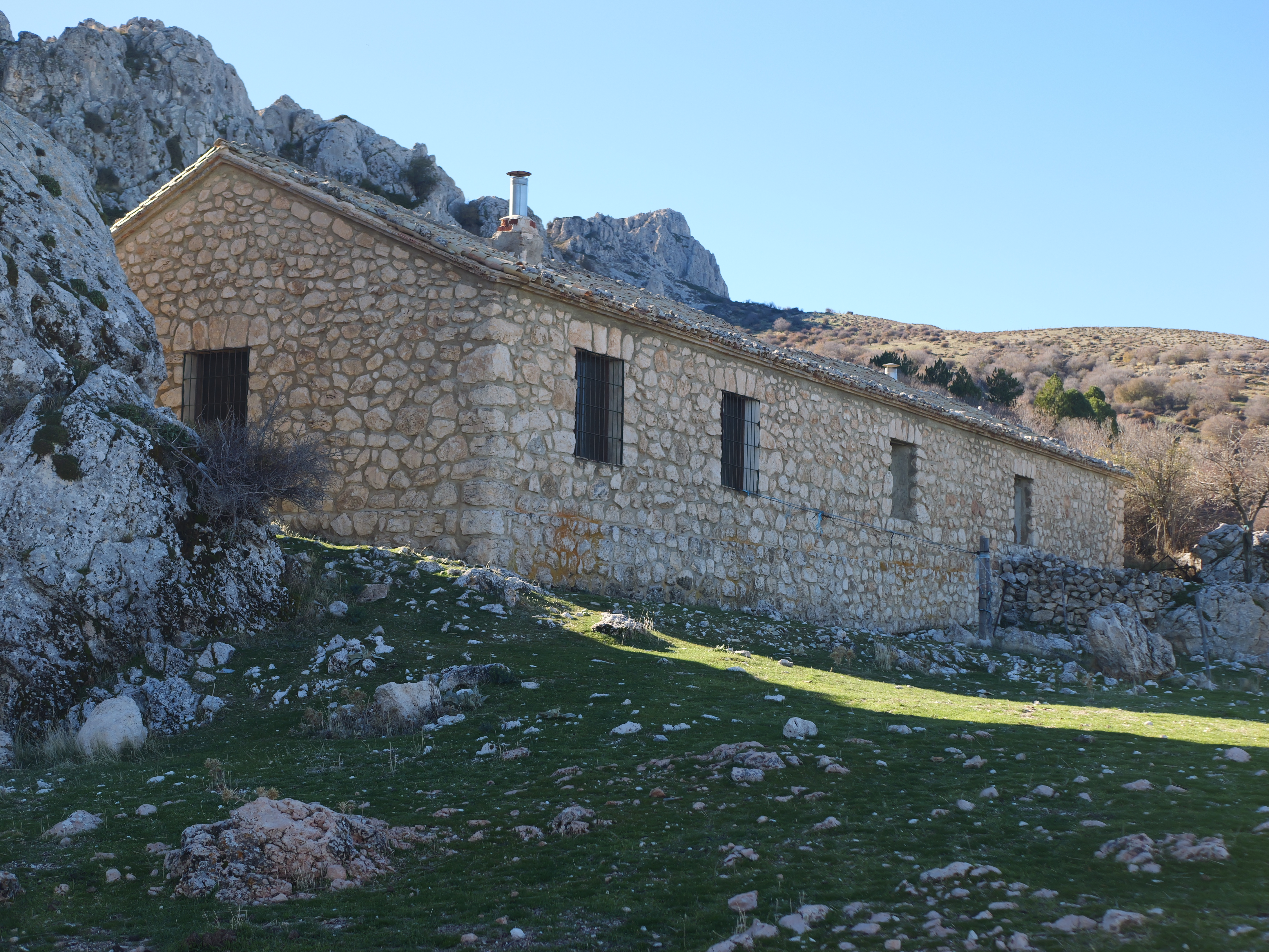 Construcción tradicional de piedra integrada en el entorno natural, rodeada de pastos y rocas, que refleja la arquitectura rural ligada a la vida en la sierra.