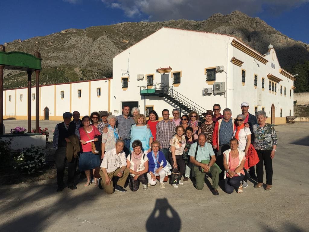 Grupo de visitantes posando frente a la almazara con la sierra al fondo, tras una actividad o visita guiada.