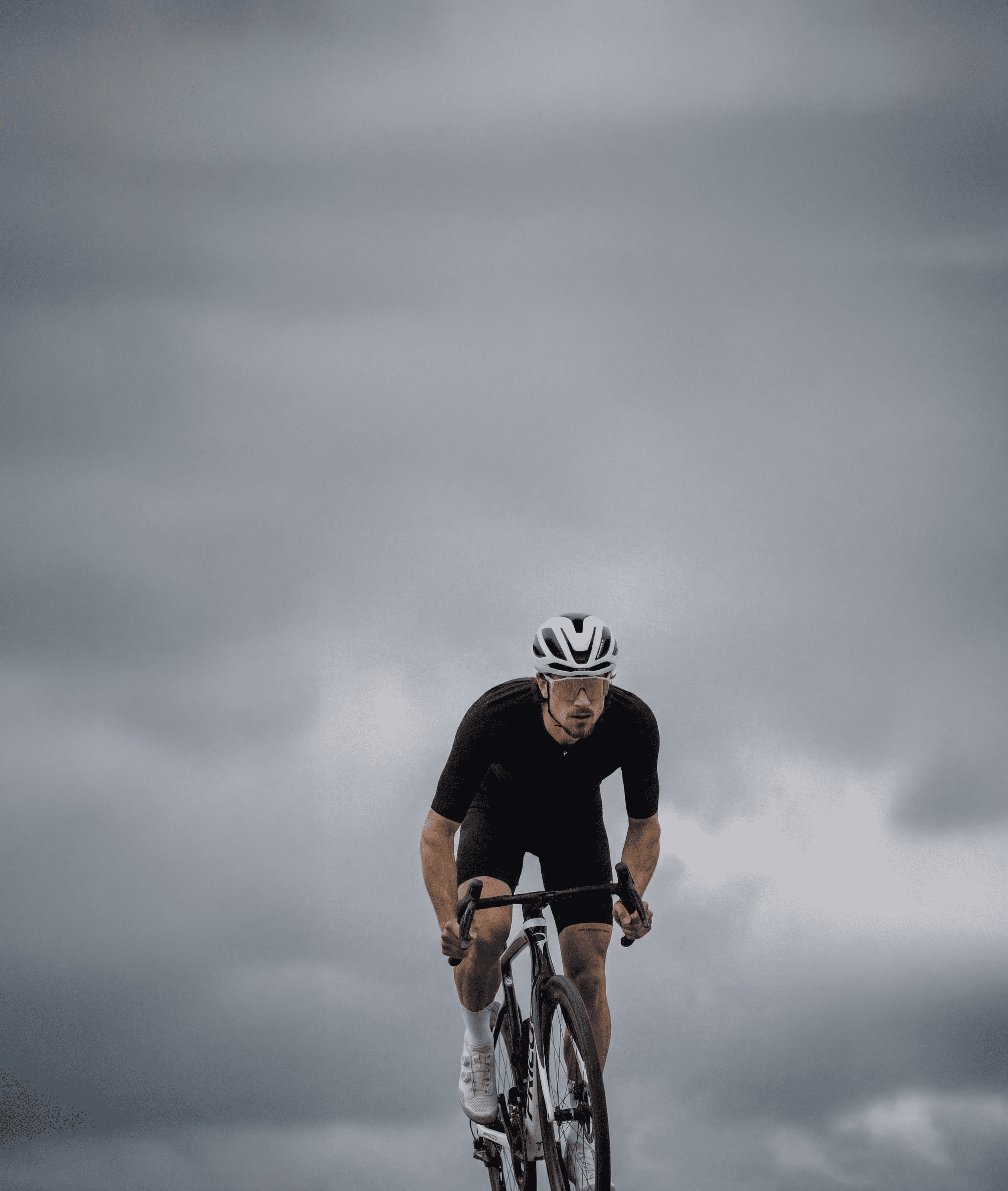 Ciclista sobre una bicicleta de carretera avanzando en solitario bajo un cielo cubierto de nubes grises. La imagen centra toda la atención en la figura del deportista y transmite sensación de esfuerzo, movimiento y superación.