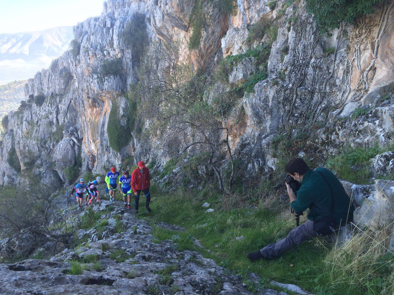 Grupo avanzando por una senda entre paredes rocosas y vegetación de montaña durante una actividad al aire libre.