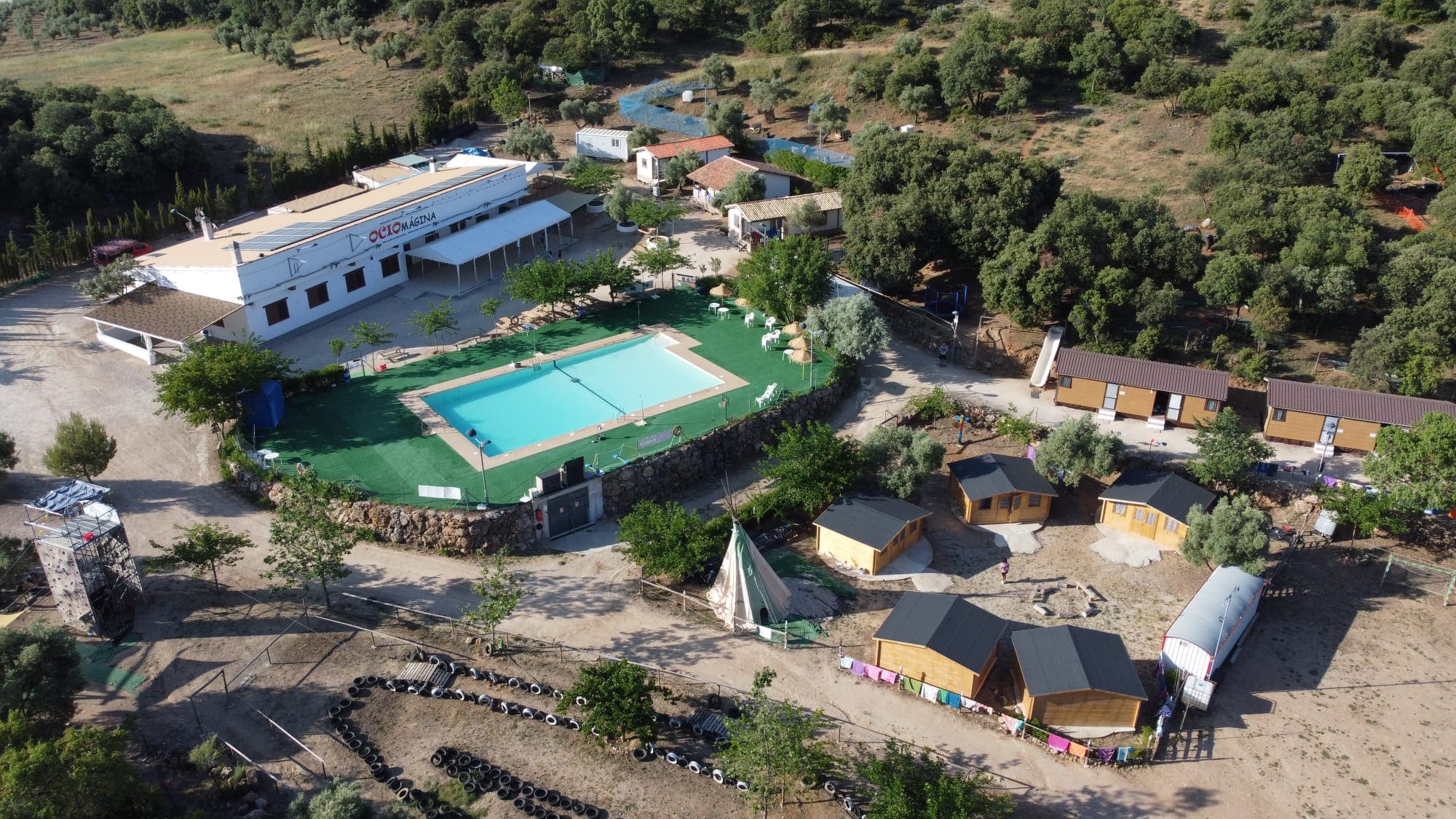 Vista general del campamento con piscina, zonas de sombra, cabañas y espacios preparados para actividades deportivas y educativas al aire libre.