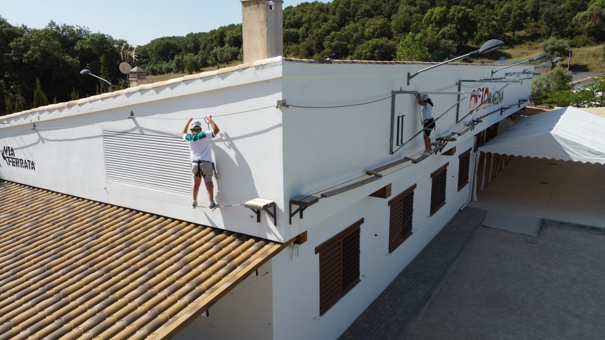 Dos personas realizando un recorrido de equilibrio y escalada tipo vía ferrata sobre una estructura elevada junto a un edificio.