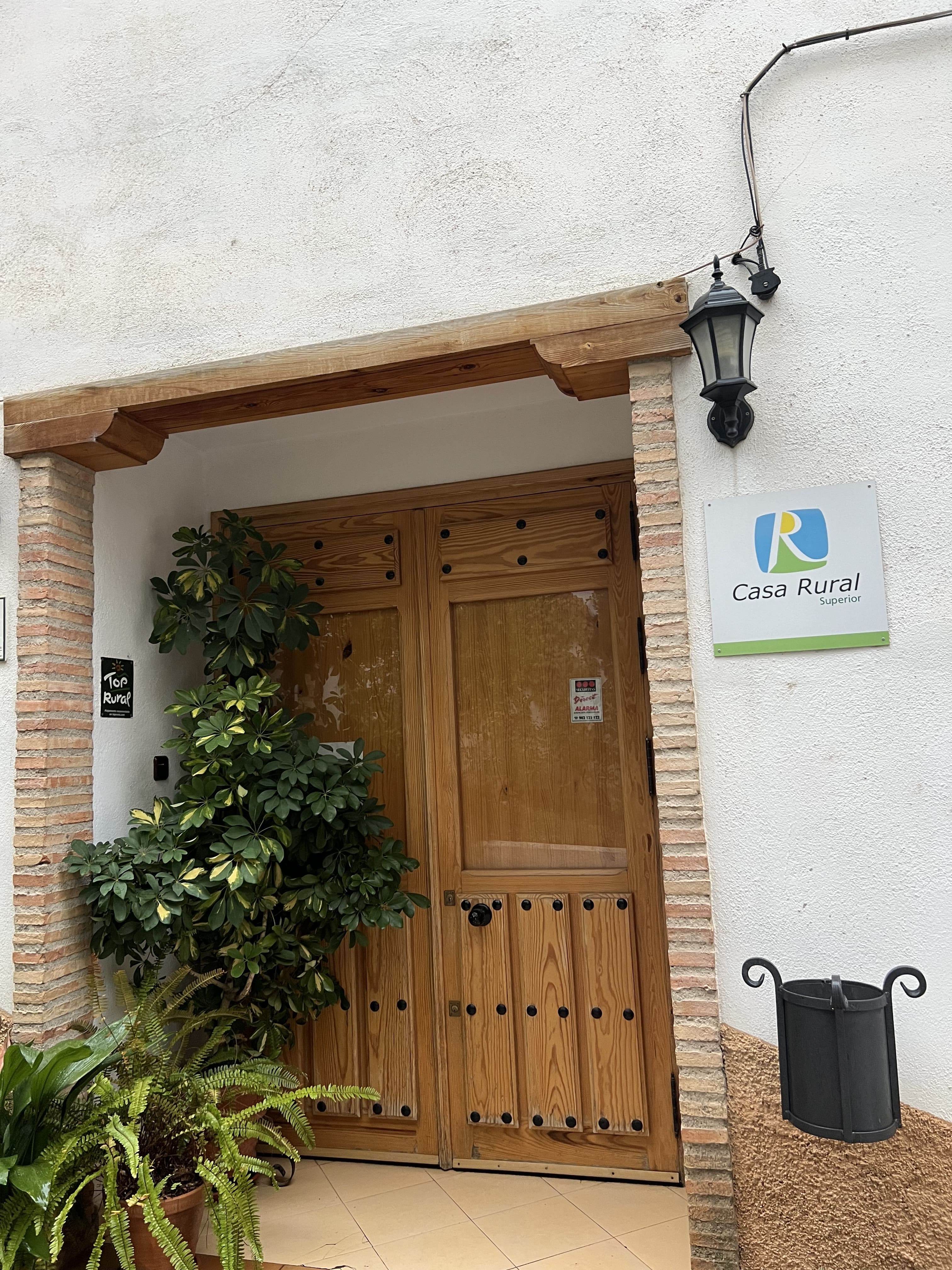 Vista de la puerta de entrada de la Casa Rural Arenaria, con un cartel que indica "Casa Rural Superior" junto a una planta decorativa. La puerta es de madera con detalles tradicionales.