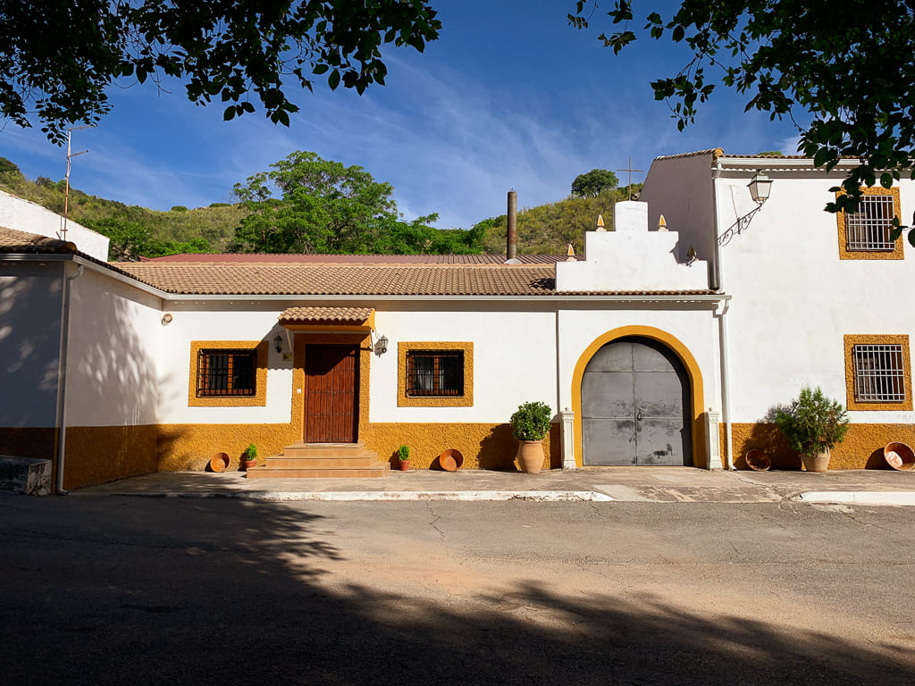Fachada principal de un cortijo andaluz con puerta de madera y gran portón, situada en un entorno rural de montaña.