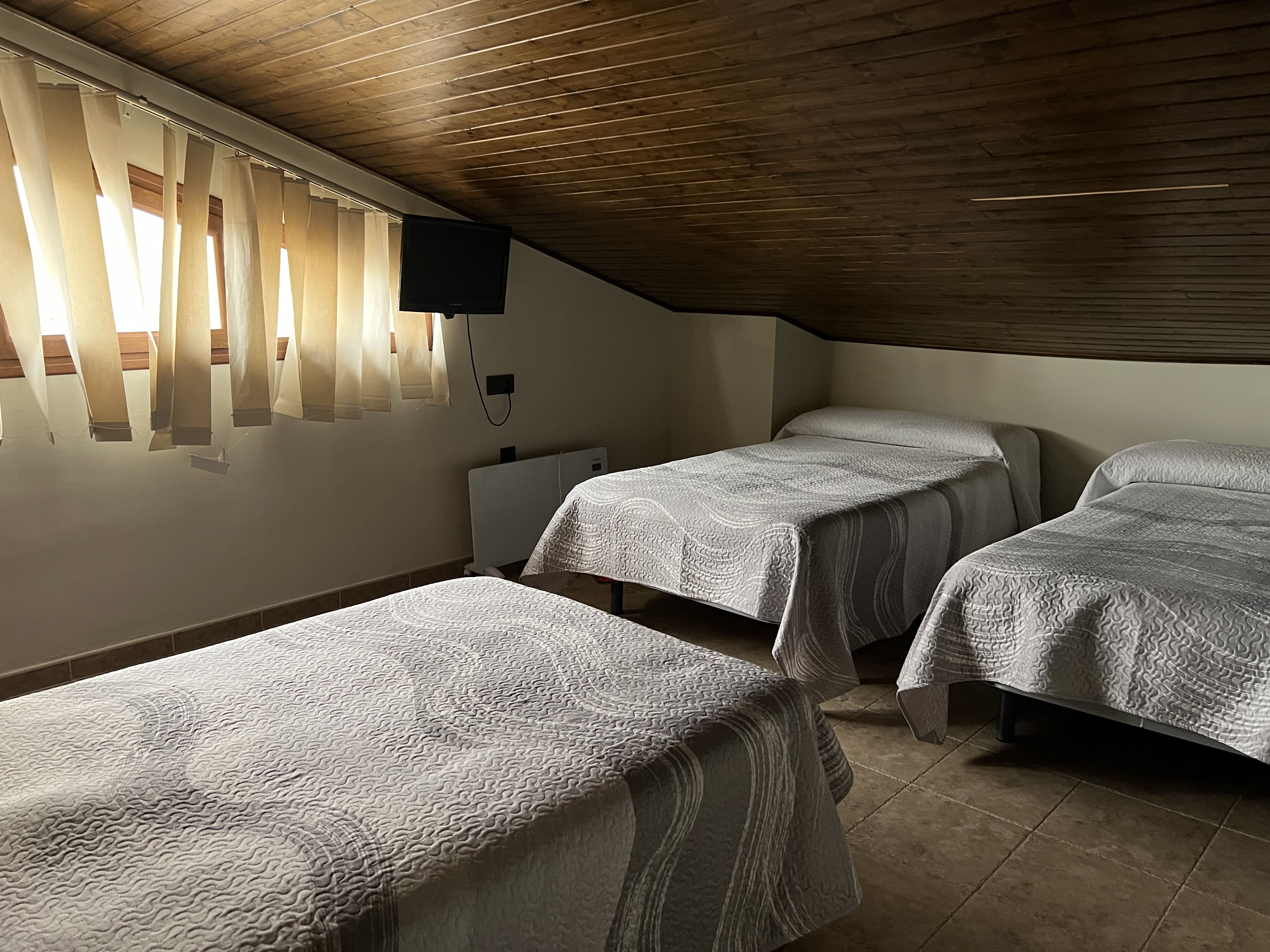Dormitorio abuhardillado con tres camas individuales, luz natural suave y decoración sencilla y acogedora.