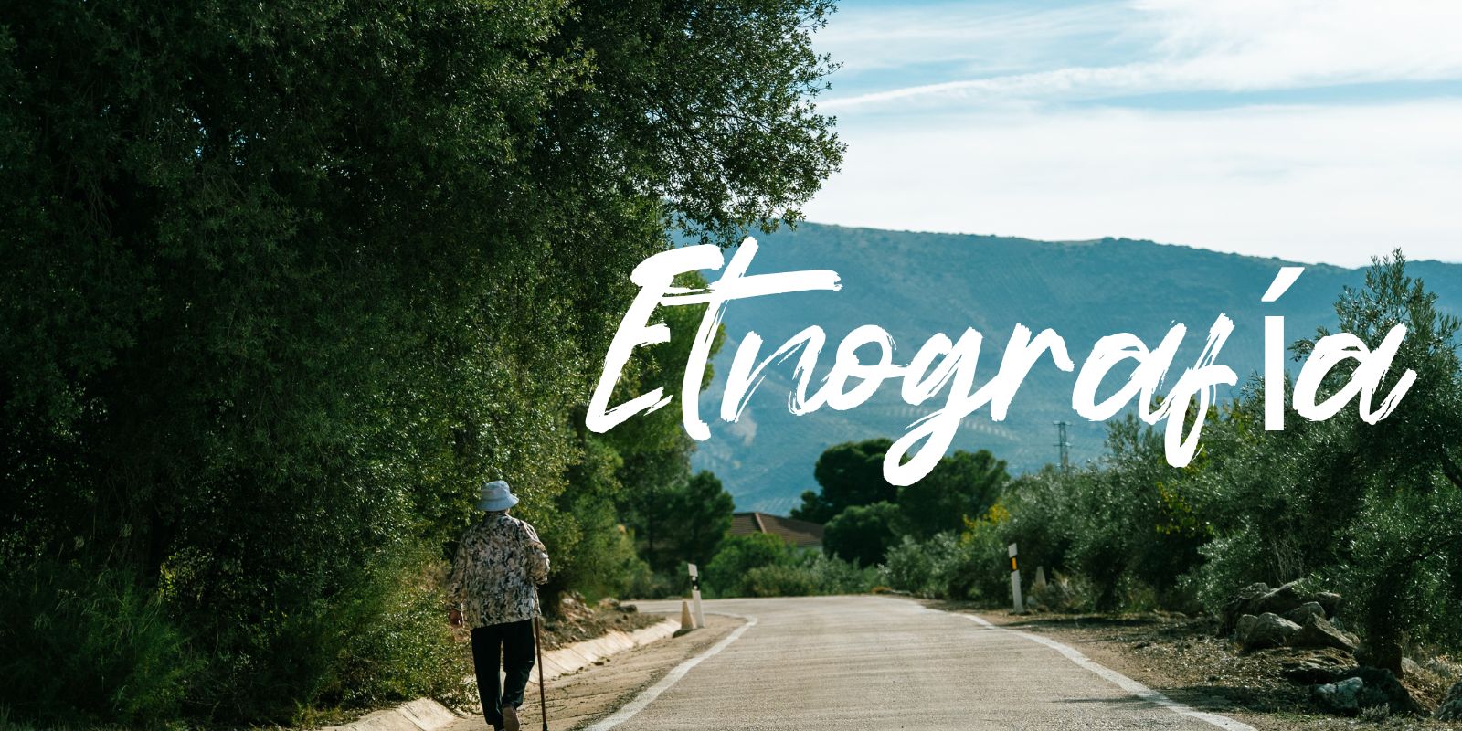 Persona caminando por una carretera rural rodeada de árboles y olivares, con montañas al fondo y la palabra “Etnografía” sobreimpresa en blanco.