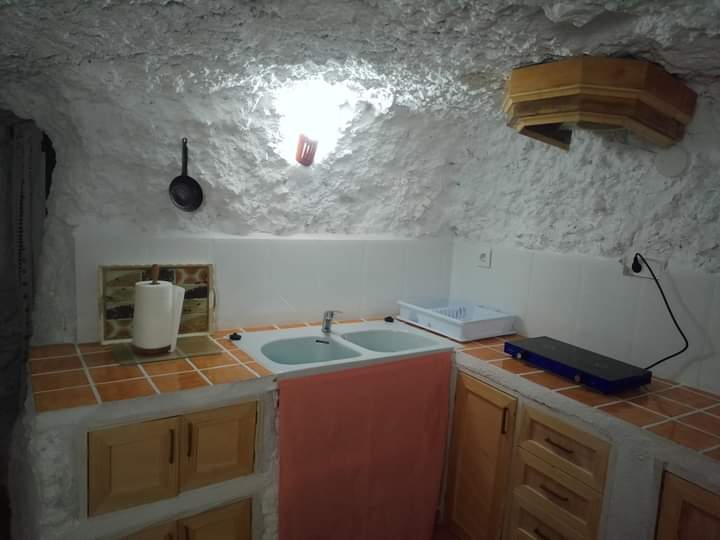 Cocina rústica excavada en la roca, con paredes blancas irregulares y mobiliario de madera. Combina sencillez y autenticidad en un ambiente acogedor.