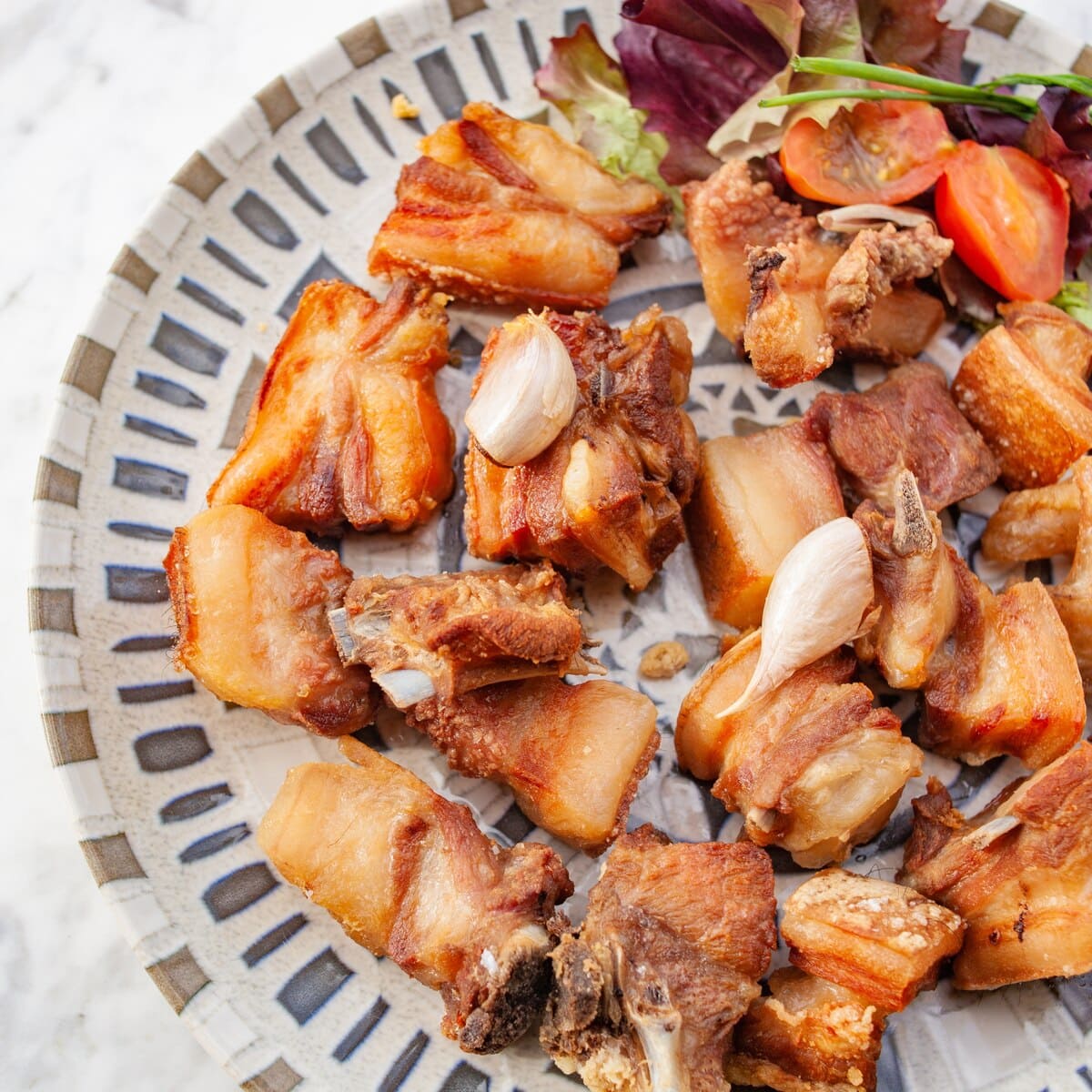 Plato visto desde arriba con varios trozos de carne frita dorada, acompañados de hojas de ensalada y dientes de ajo.