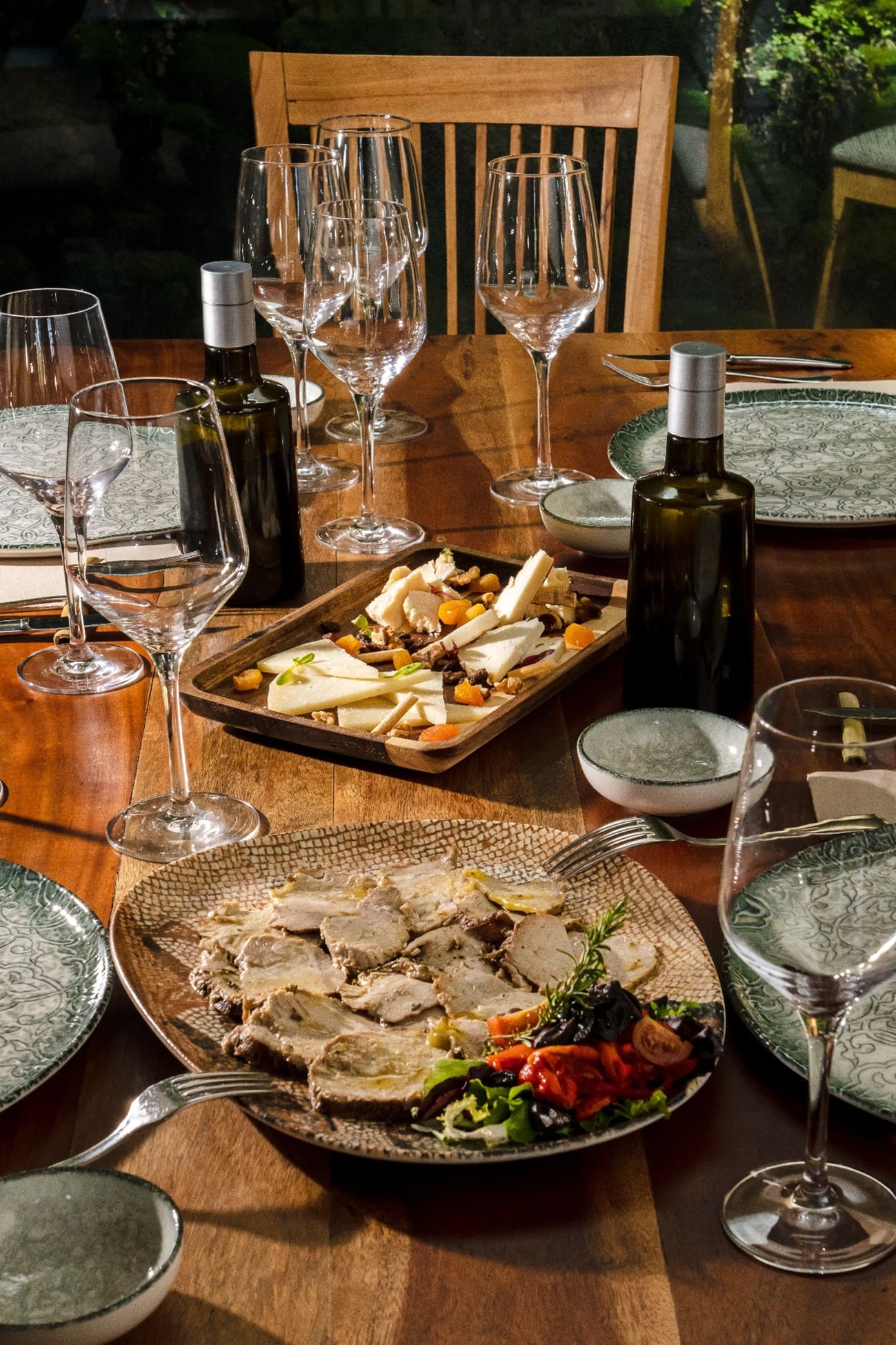 Mesa de restaurante con platos de comida, botellas de aceite y copas de vino preparadas para una comida.