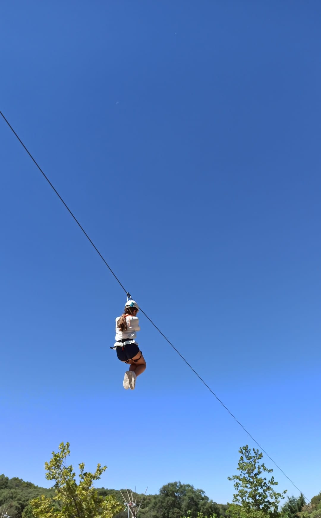 Persona deslizándose por una tirolina bajo un cielo despejado, en un entorno natural de sierra.