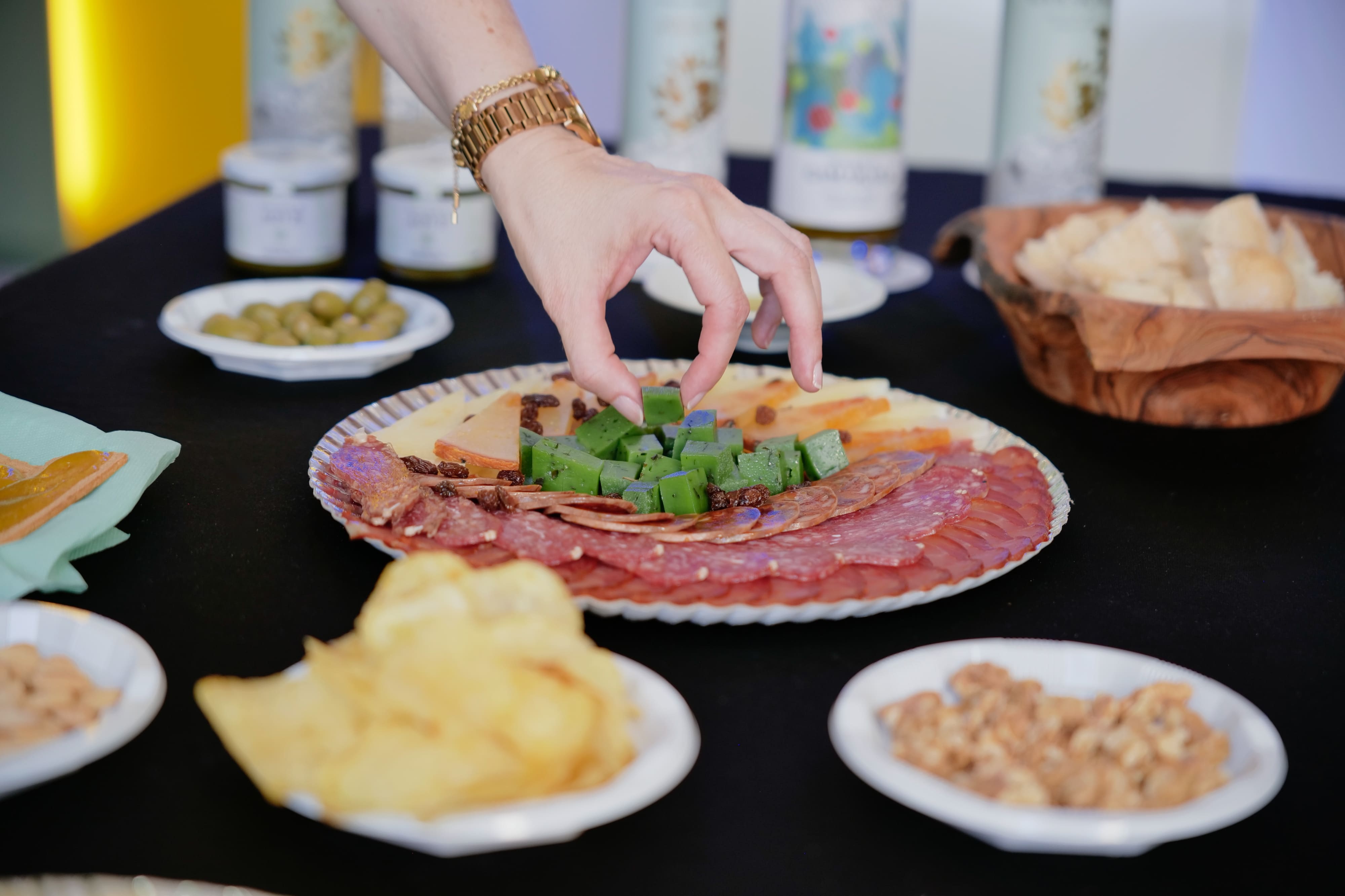 Plato de embutidos, queso y aperitivos acompañado de aceite de oliva, mientras una mano toma un alimento para degustar.