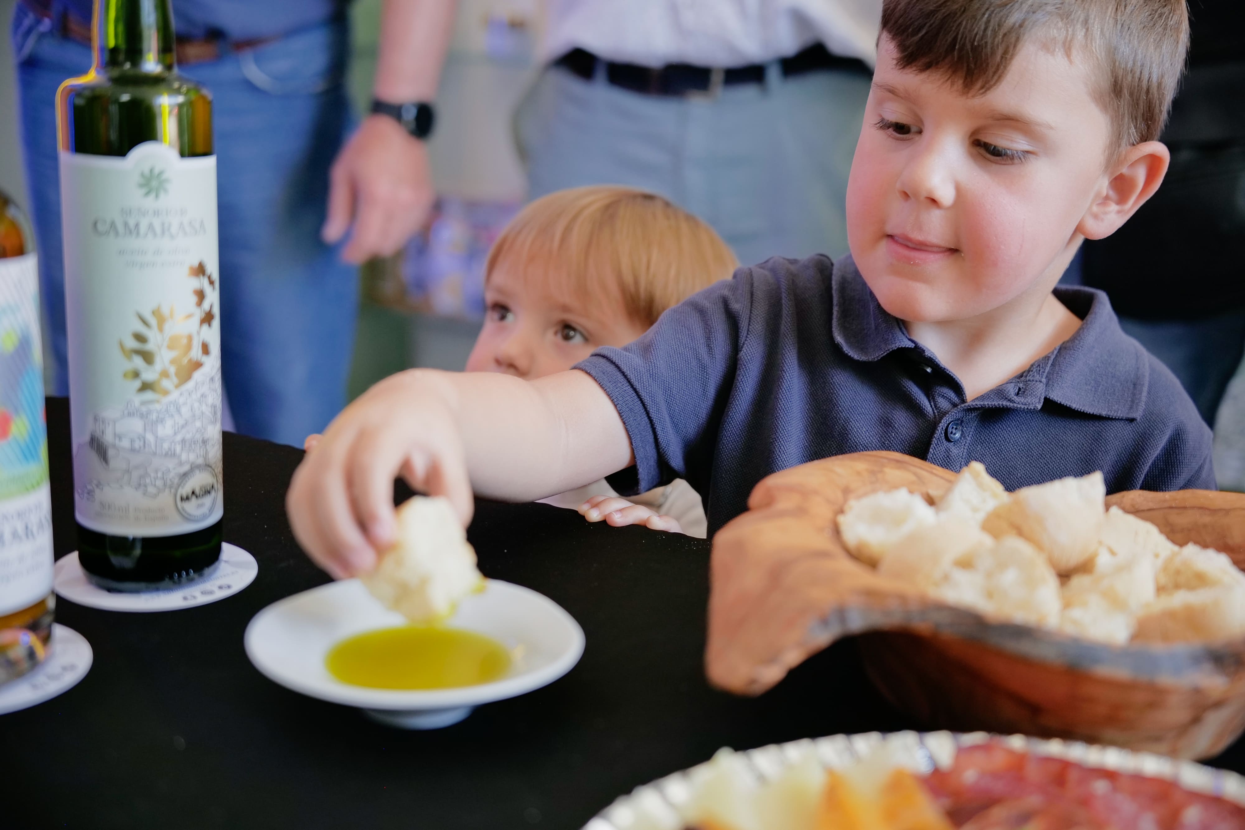 Niño mojando pan en aceite de oliva durante una degustación en interior.
