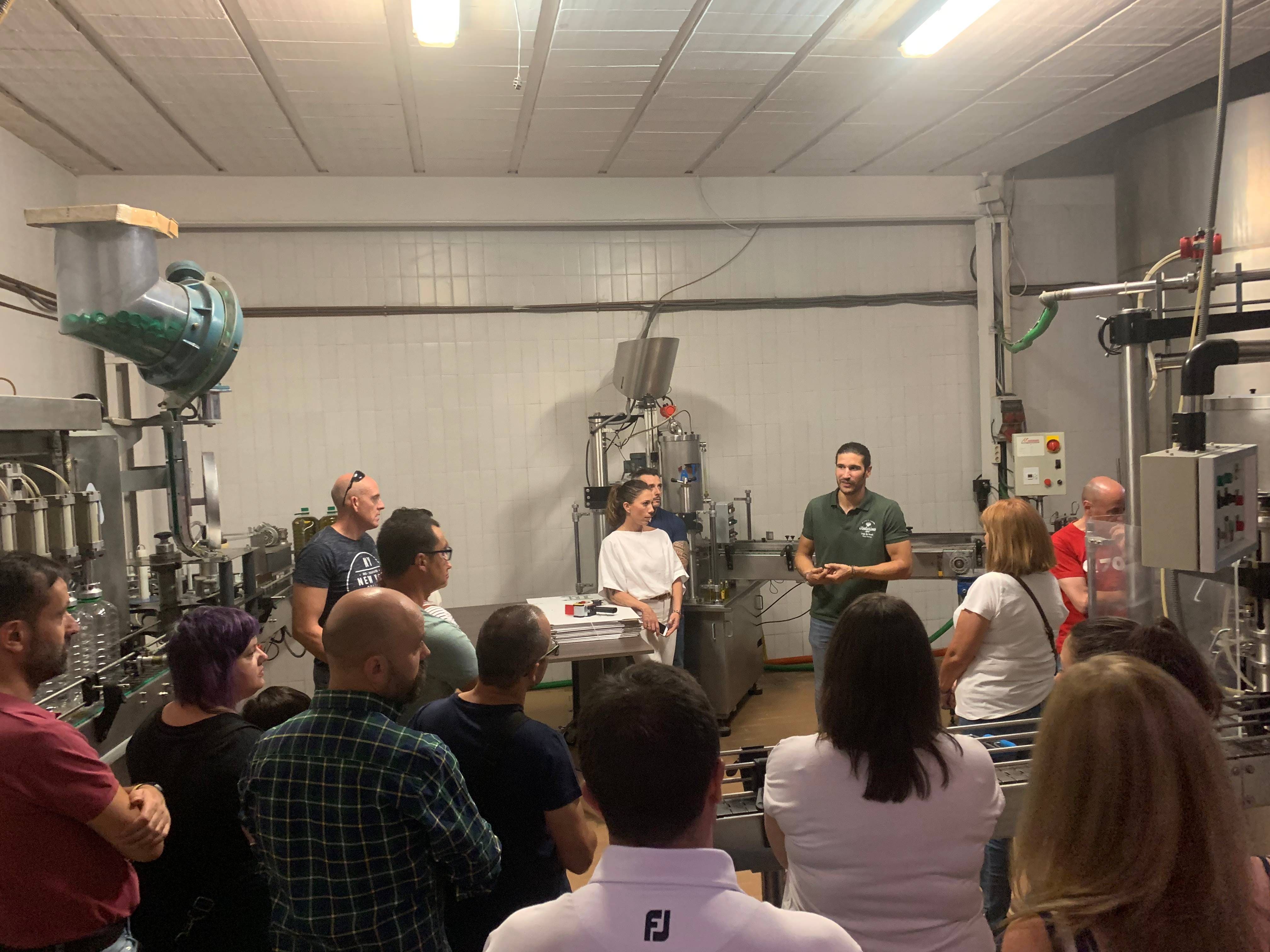 Grupo de visitantes escuchando a un guía en el interior de una almazara junto a maquinaria de producción de aceite.