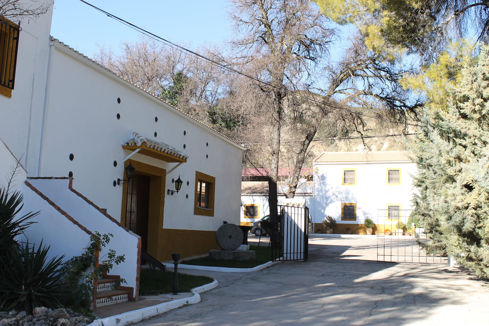 Entrada a un cortijo andaluz con casas blancas, patio abierto y entorno tranquilo rodeado de árboles.