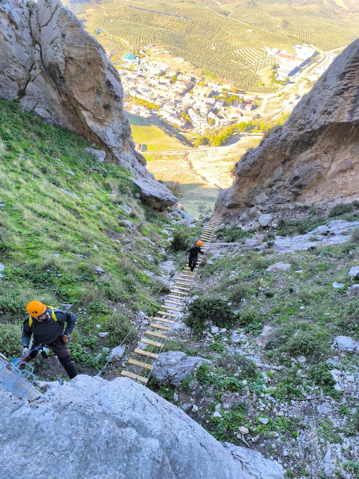 os participantes avanzan por una vía ferrata equipada con peldaños y cables, atravesando un tramo elevado entre paredes de roca con el valle al fondo.
