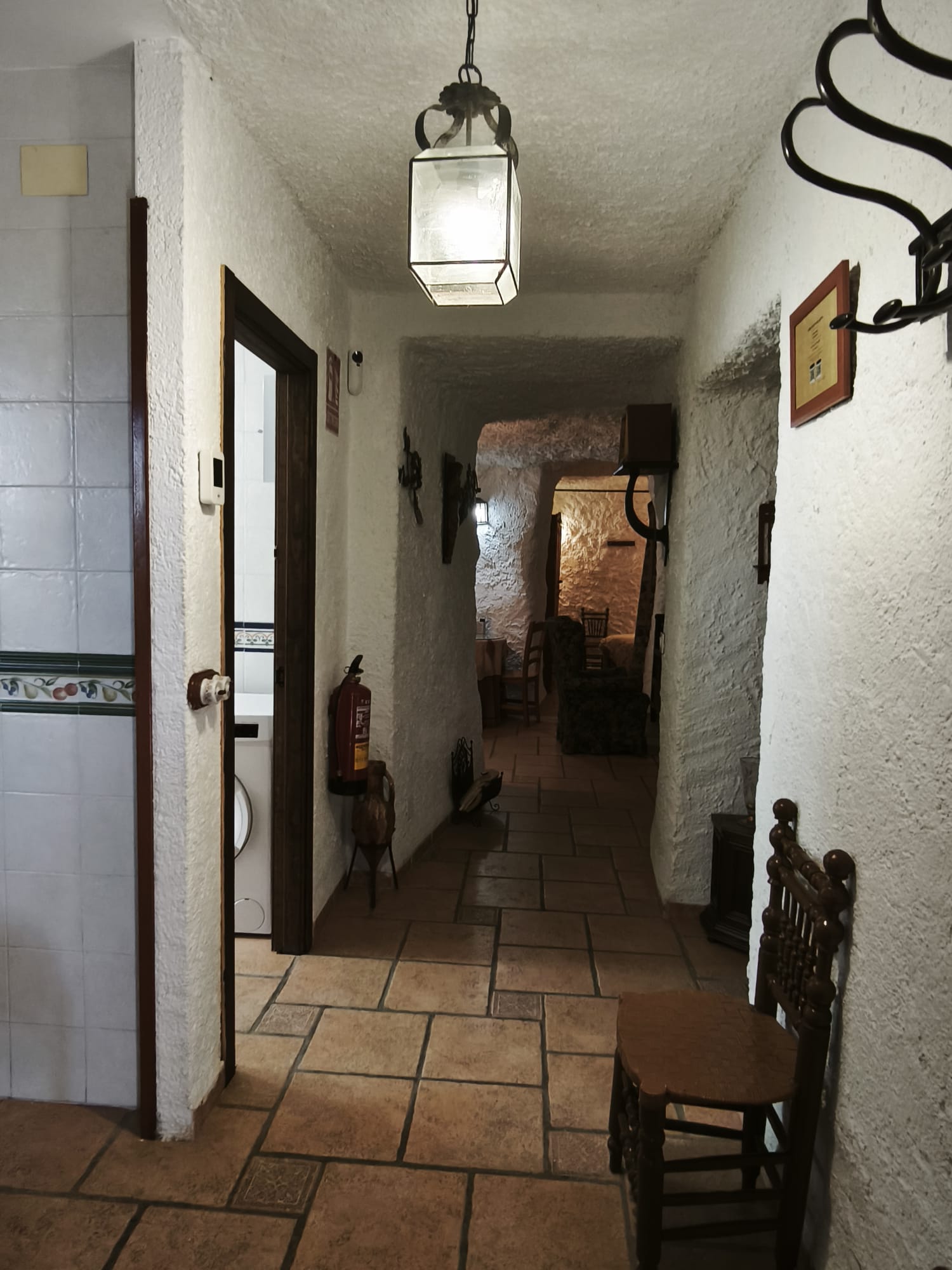 Pasillo interior con paredes encaladas y formas suaves propias de una casa cueva. La iluminación cálida y el suelo de barro refuerzan la sensación de acogida y tradición.