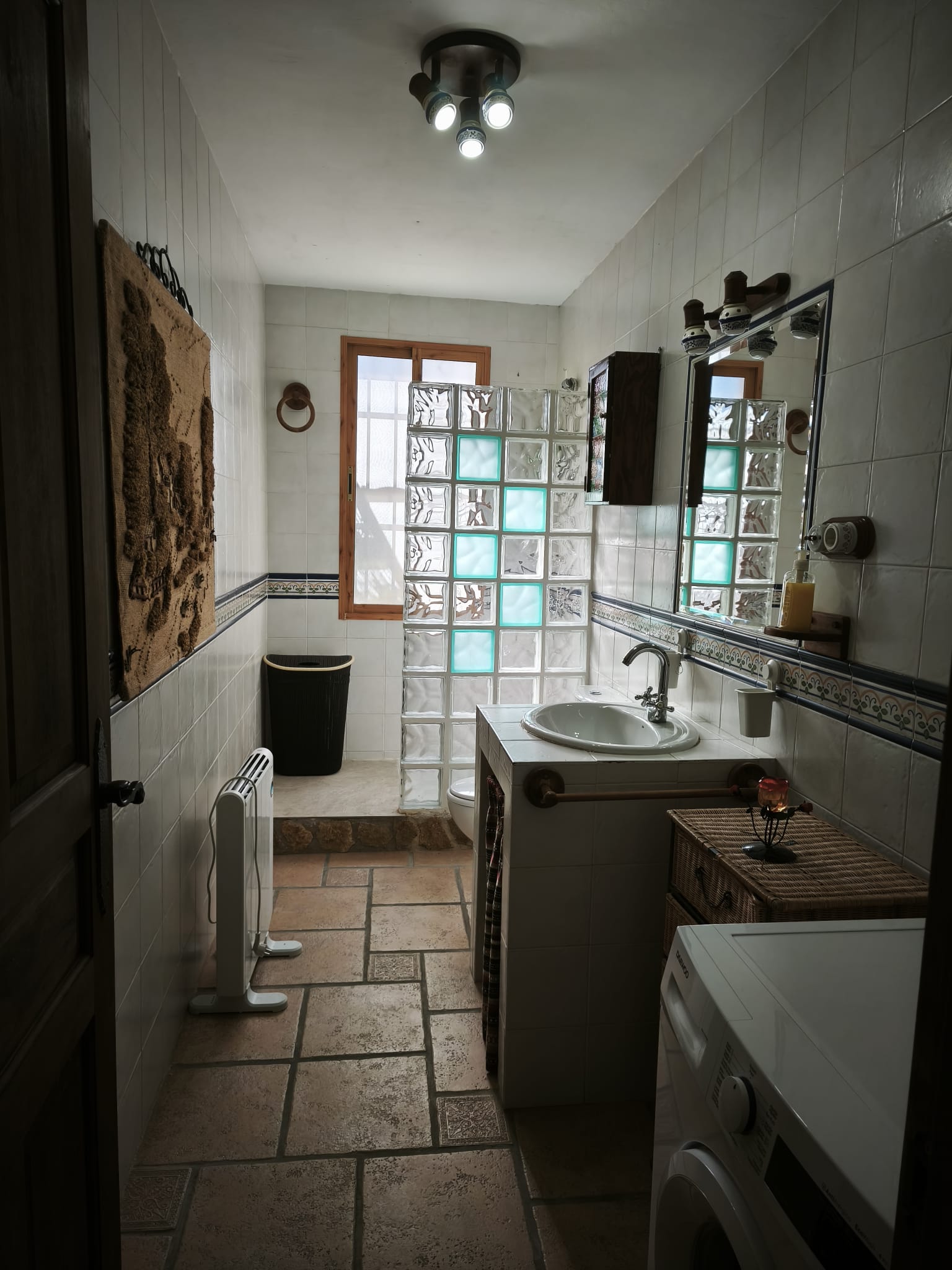 Baño amplio y luminoso, con azulejos claros y una zona de ducha separada por bloques de vidrio. Un espacio funcional que combina comodidad y estilo sencillo.