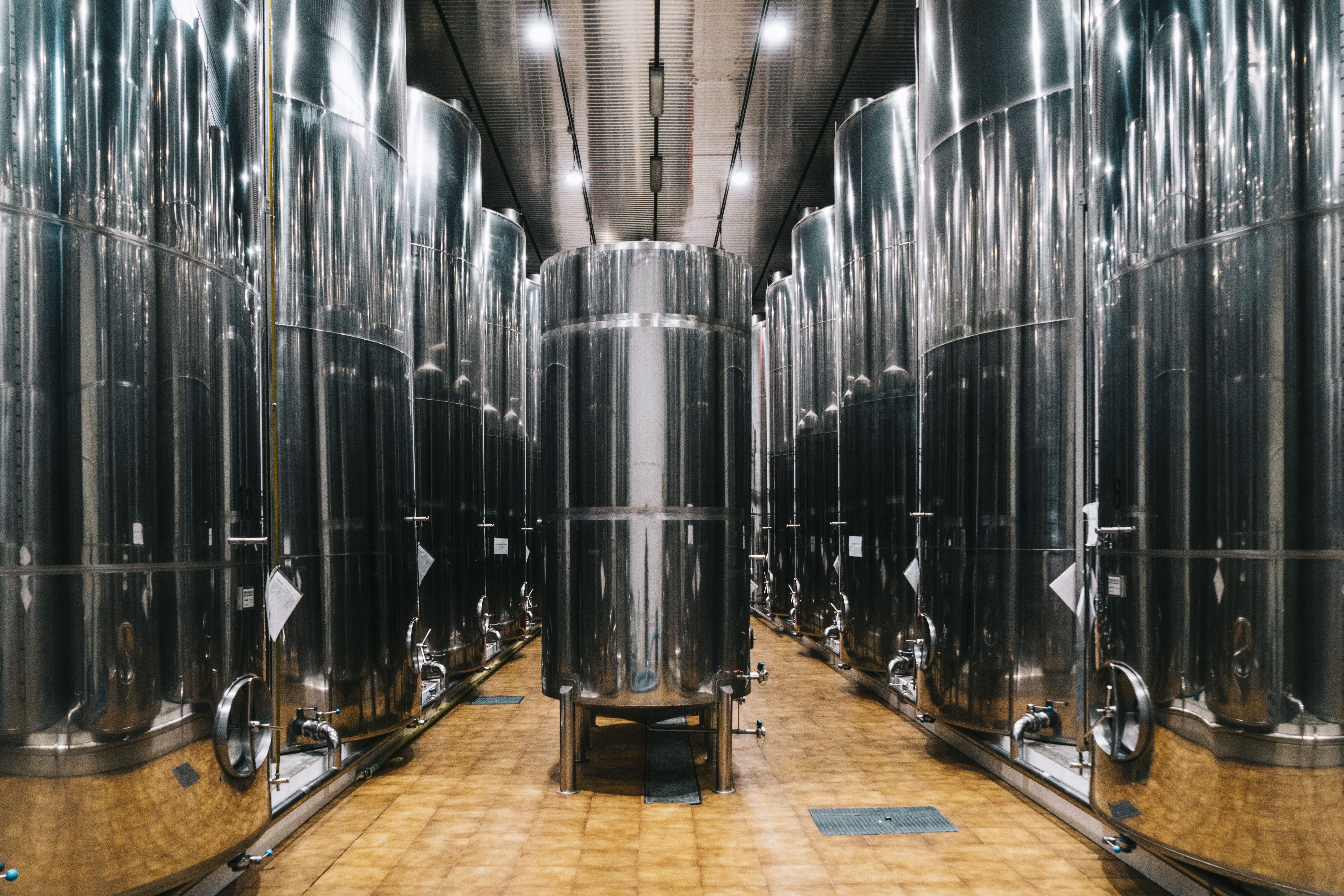 Interior de una bodega de aceite con grandes depósitos cilíndricos de acero inoxidable alineados a ambos lados de un pasillo central. La iluminación refleja el brillo metálico de los tanques, transmitiendo sensación de limpieza, orden y cuidado en la conservación del aceite de oliva virgen extra.
