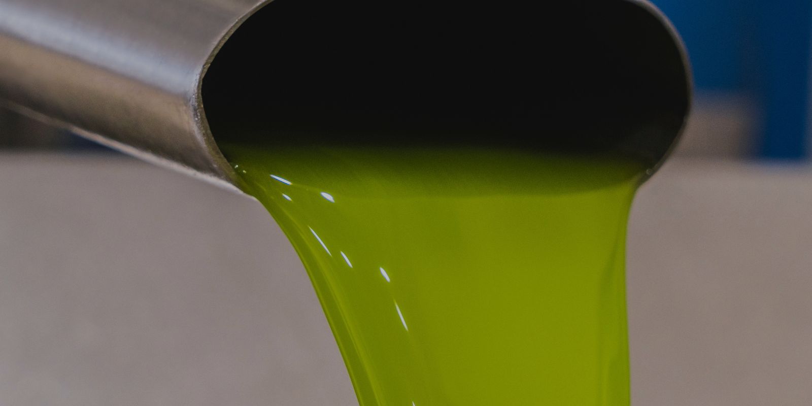 Chorro continuo de aceite de oliva virgen extra recién extraído cayendo desde una boquilla metálica. El aceite presenta un color verde intenso y luminoso, símbolo de frescura y calidad. El fondo desenfocado centra la atención en la fluidez y pureza del aceite.