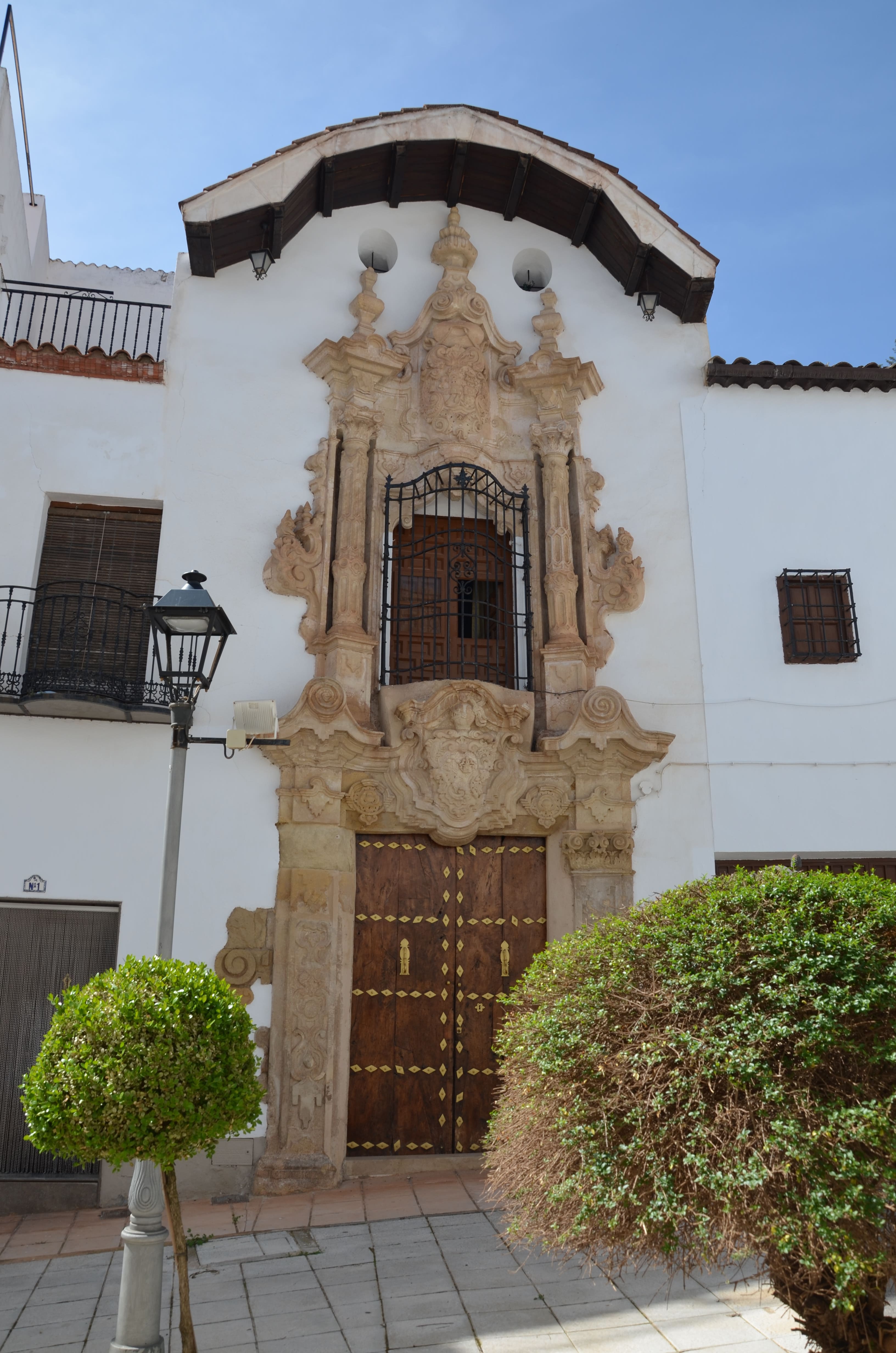 Portada barroca del antiguo hospital, con balcón central enrejado y escudo tallado sobre la puerta de madera.