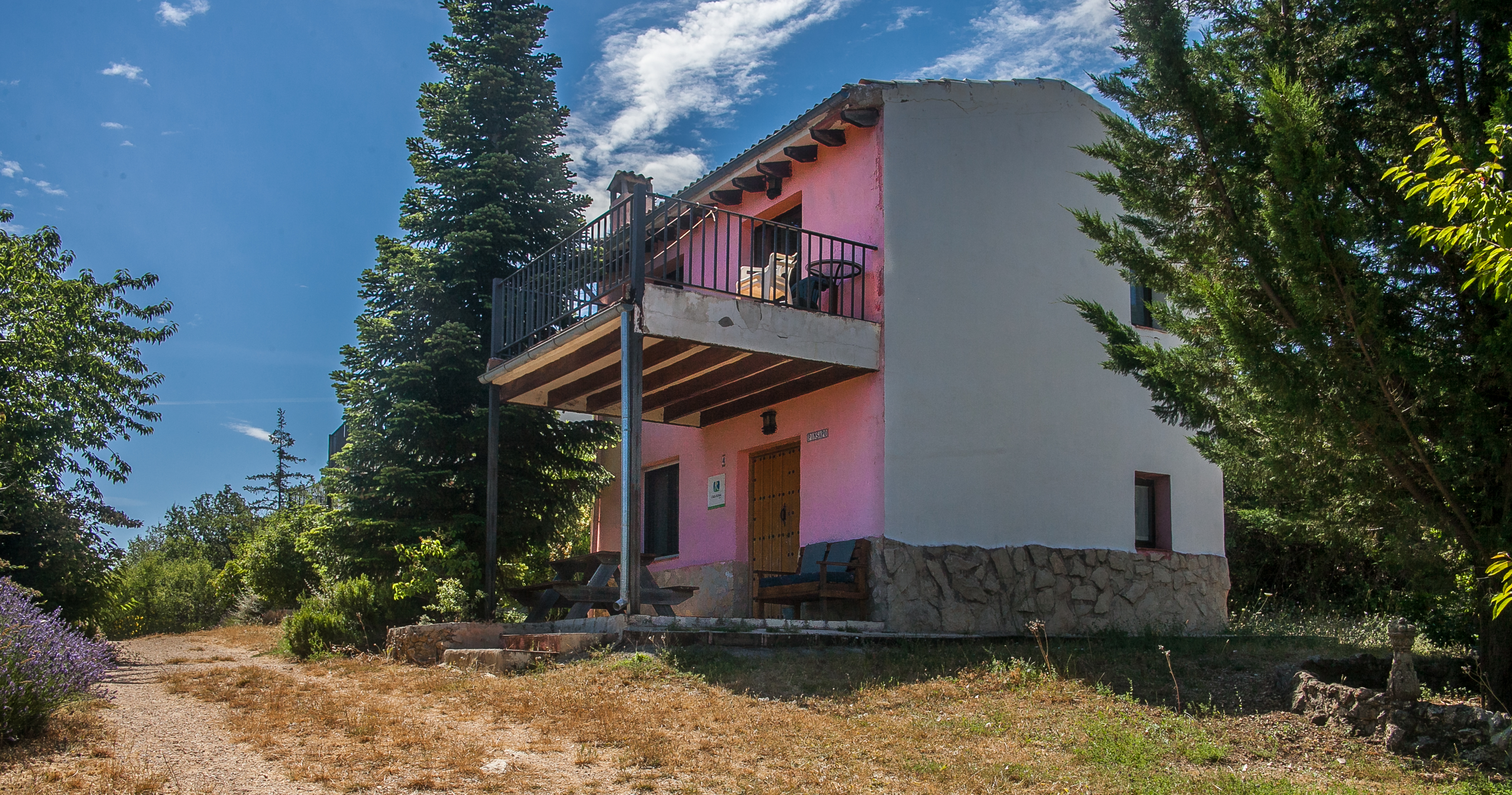 Vivienda de tonos claros con terraza elevada y zona exterior con mesa, integrada entre arbolado. Un espacio que invita a disfrutar del aire libre en un entorno tranquilo.