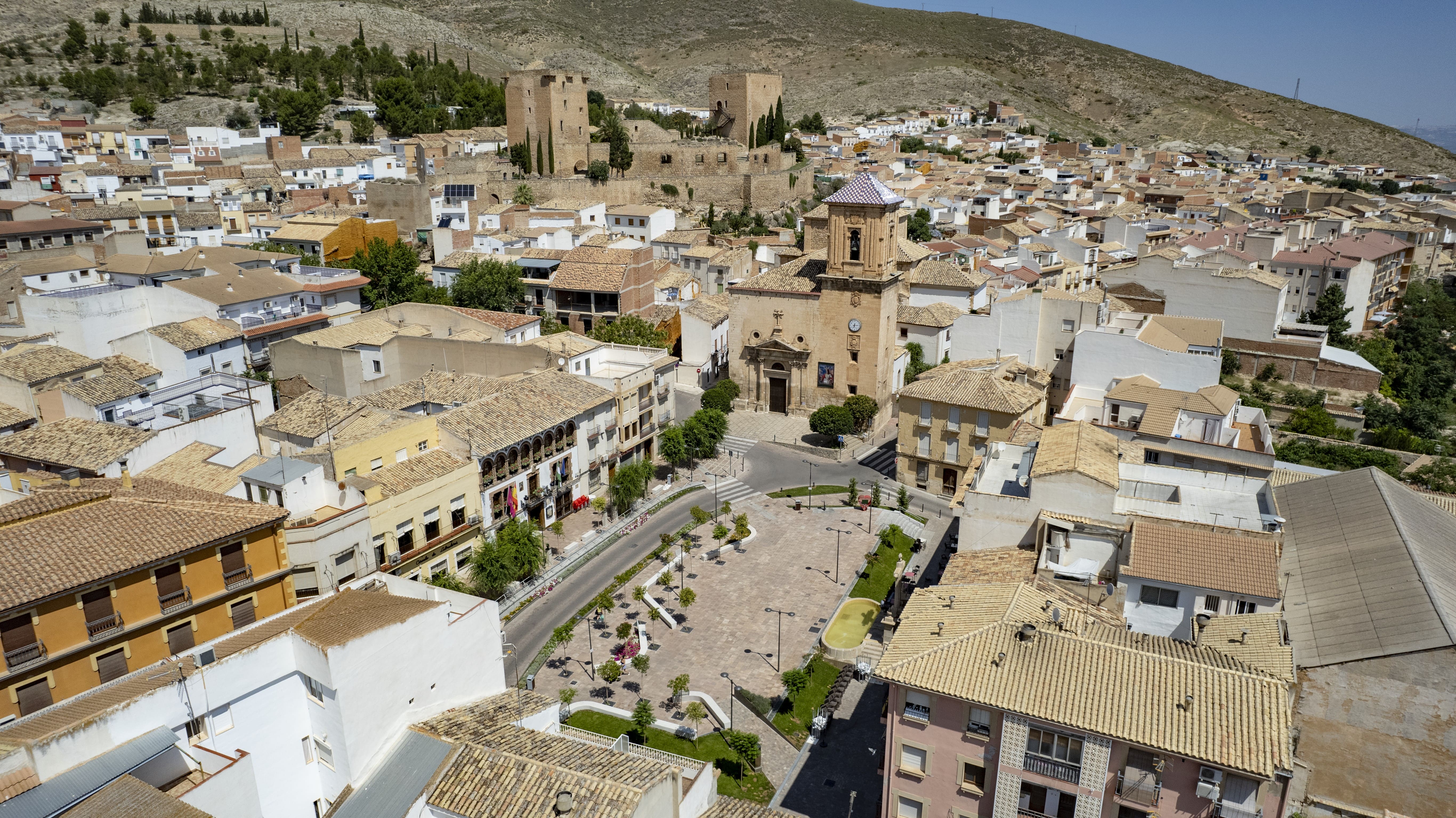 Vista aérea del centro de Jódar, con la iglesia y la plaza principal en primer plano, y el castillo elevándose sobre el conjunto urbano al fondo.