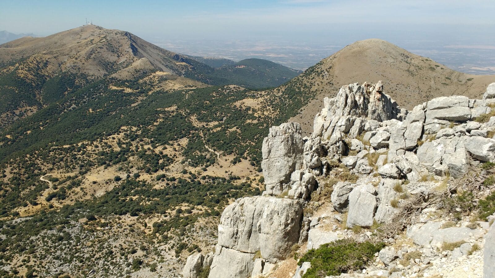 Paisaje de montaña con formaciones rocosas en primer plano y amplias laderas al fondo. Se aprecian cumbres redondeadas, vegetación dispersa y una gran sensación de amplitud y altura.