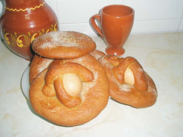 Hornazos tradicionales de masa dorada, decorados con huevos cocidos enteros y espolvoreados con azúcar. Están presentados en un plato, junto a una jarra y una taza de barro, evocando una elaboración casera típica de Pascua.