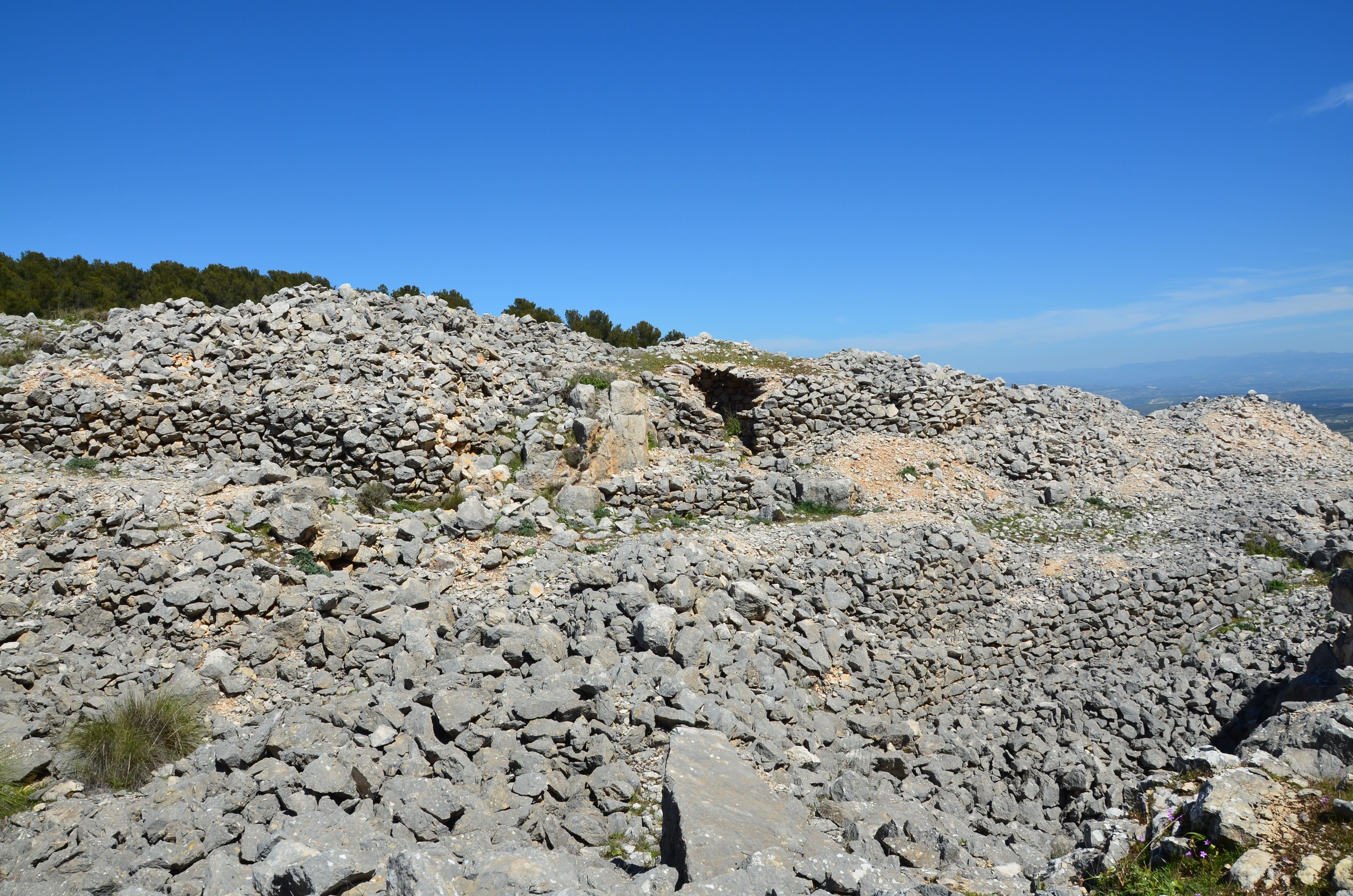 Detalle del entorno rocoso de Los Caracoles, con antiguas estructuras de piedra seca en la ladera y vistas abiertas hacia el paisaje de Sierra Mágina. El cielo azul y la amplitud del terreno destacan el carácter natural y etnográfico del lugar.