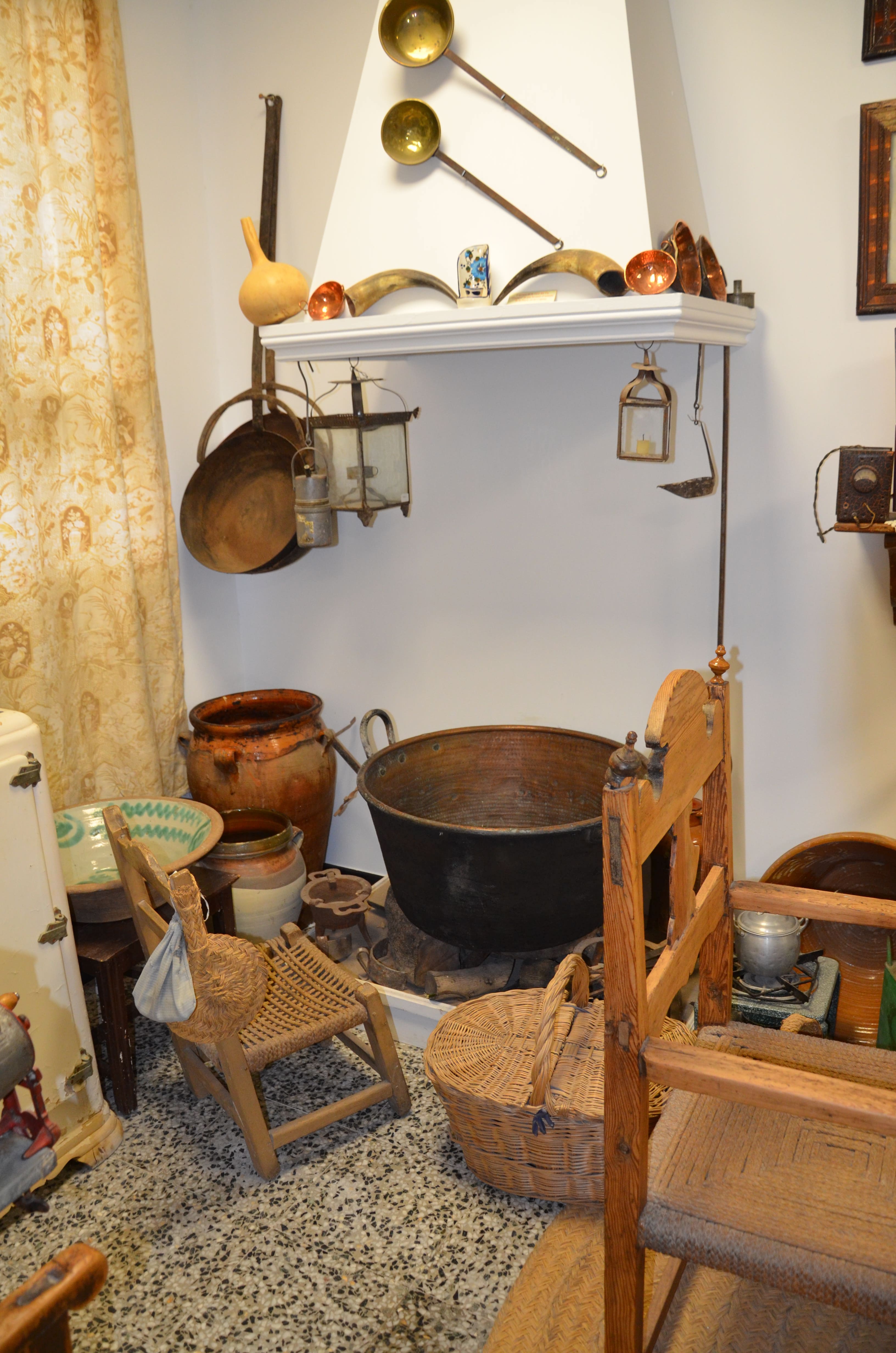 Rincón expositivo con utensilios domésticos y tradicionales, como cestos de mimbre, recipientes de cerámica, calderos, lámparas, cucharones y otros objetos utilizados en la vida cotidiana.