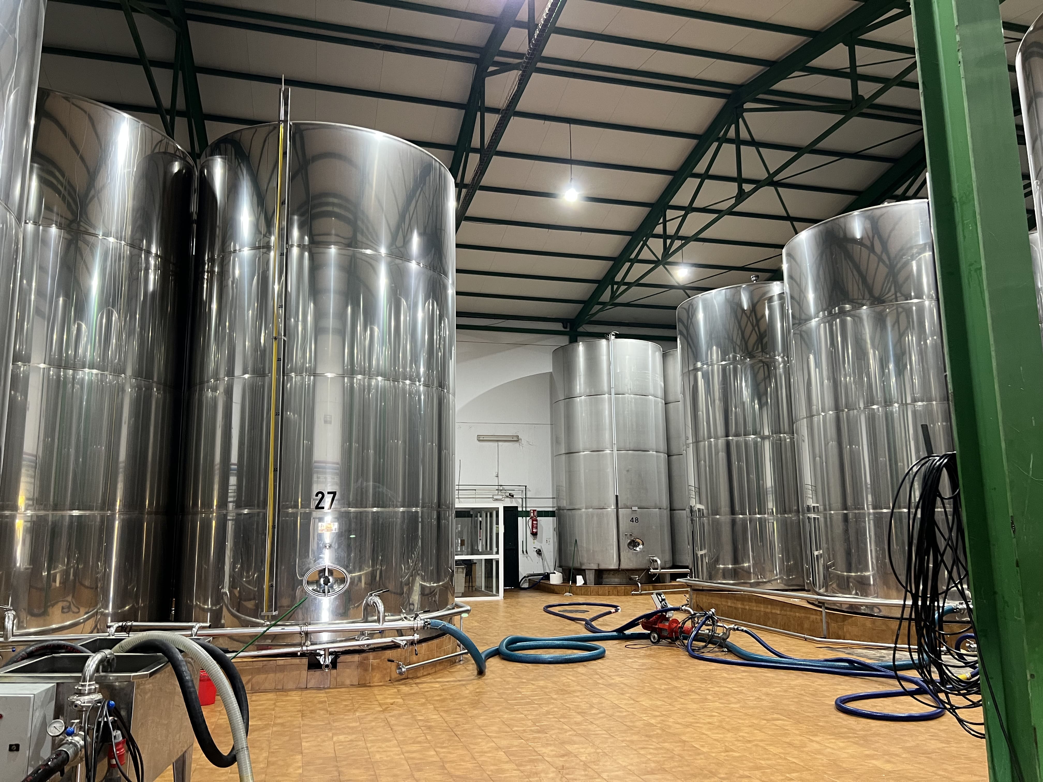Interior de una almazara con grandes depósitos metálicos de acero inoxidable, conducciones y mangueras utilizadas en el proceso de almacenamiento del aceite.