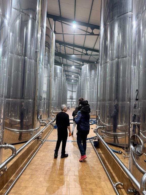 Pasillo entre grandes depósitos metálicos donde se almacena el aceite, con dos personas recorriendo las instalaciones.