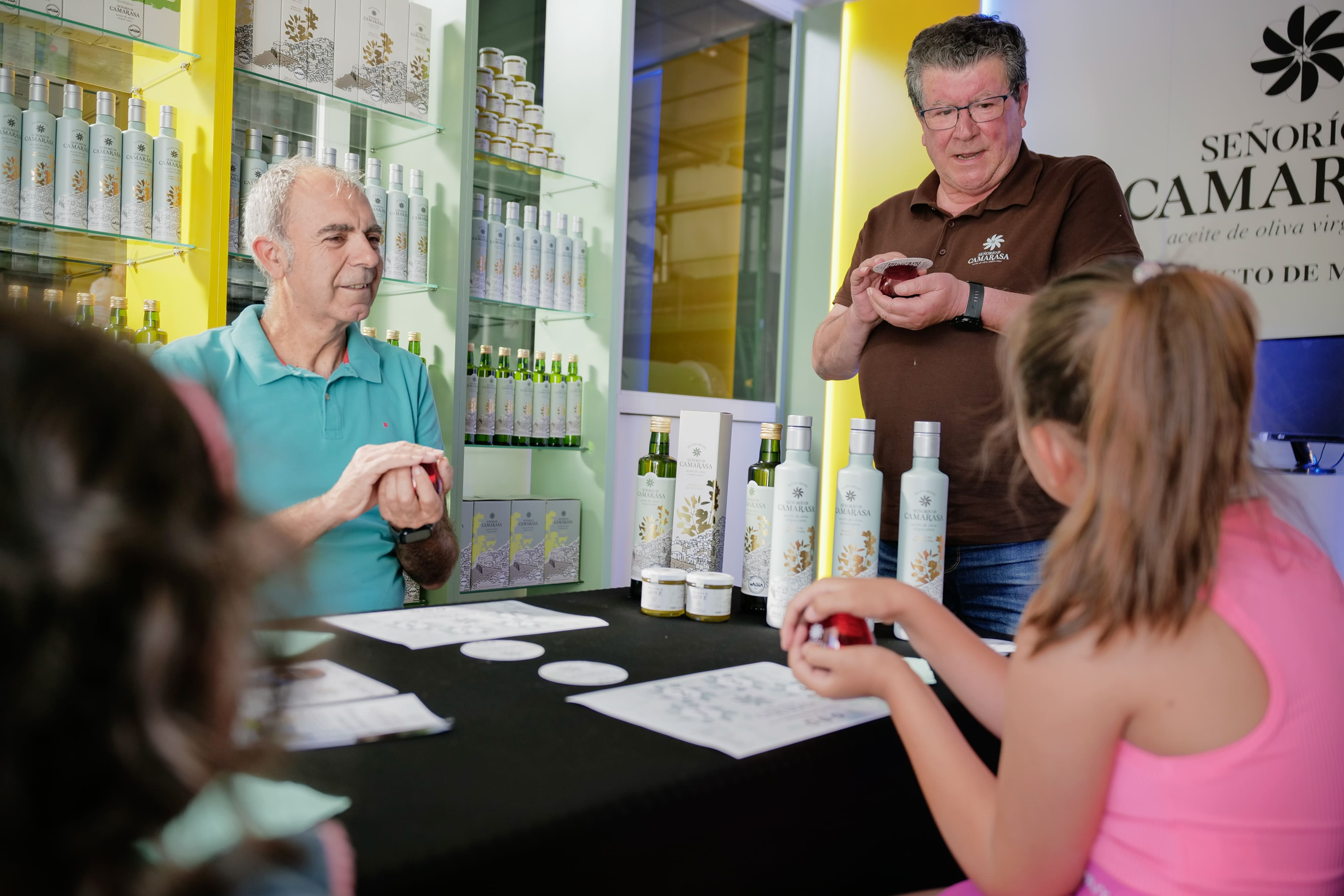 Grupo de visitantes durante una actividad de degustación en Señorío de Camarasa, con botellas de aceite expuestas al fondo mientras dos responsables explican el producto en una sala de la almazara.